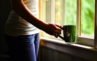 person holding green ceramic mug near window